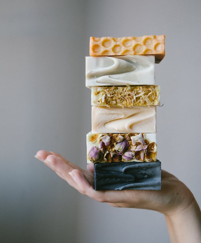 A stack of artisanal organic soaps held by a hand, showcasing natural ingredients.